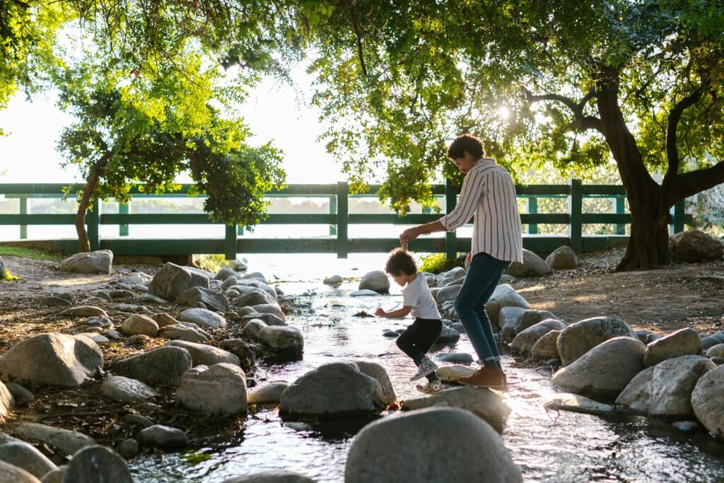 A joyful mother and son hopping over river stones during a summer walk in the park.