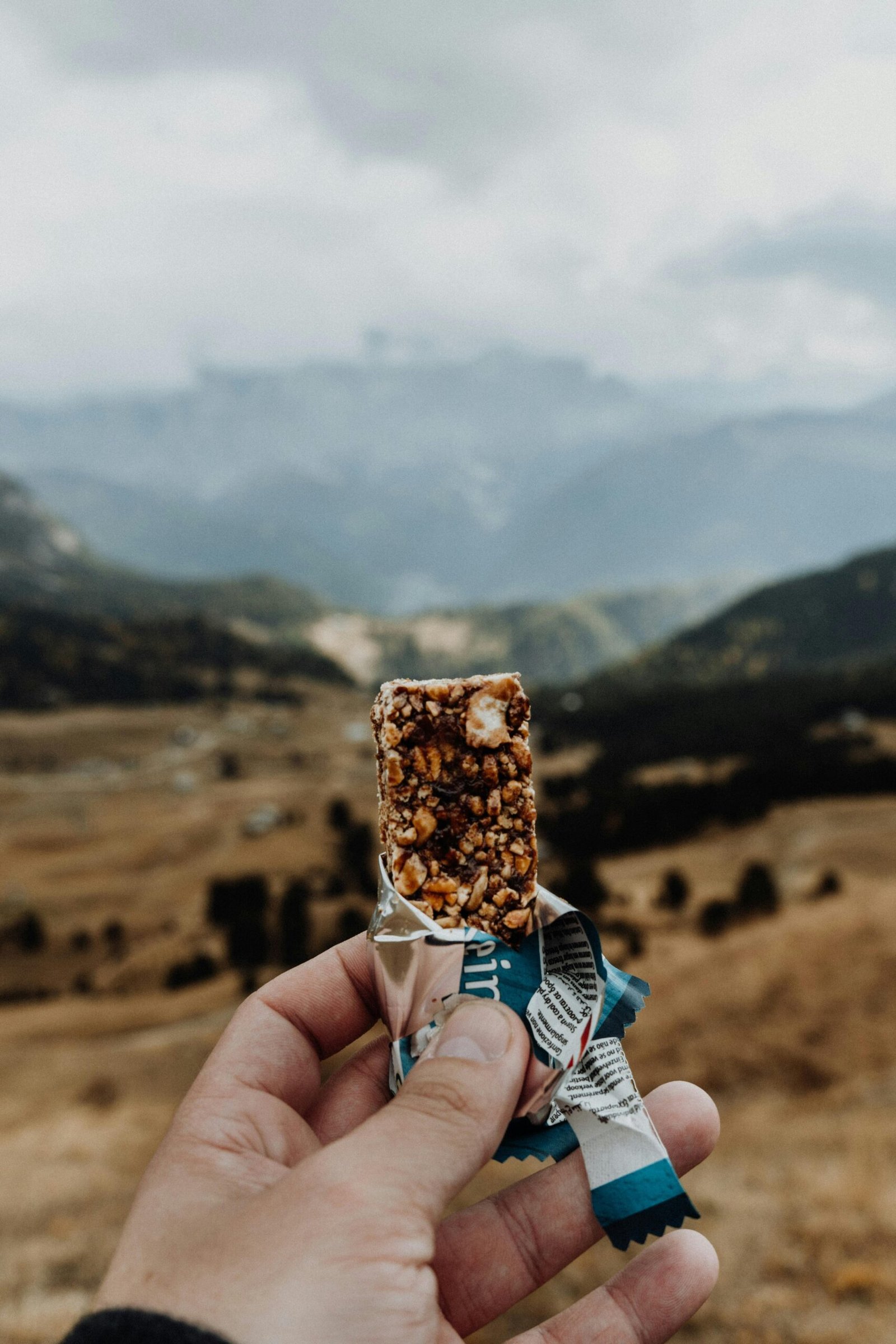Person holding a cereal bar with a mountainous landscape in Trentino, Italy.