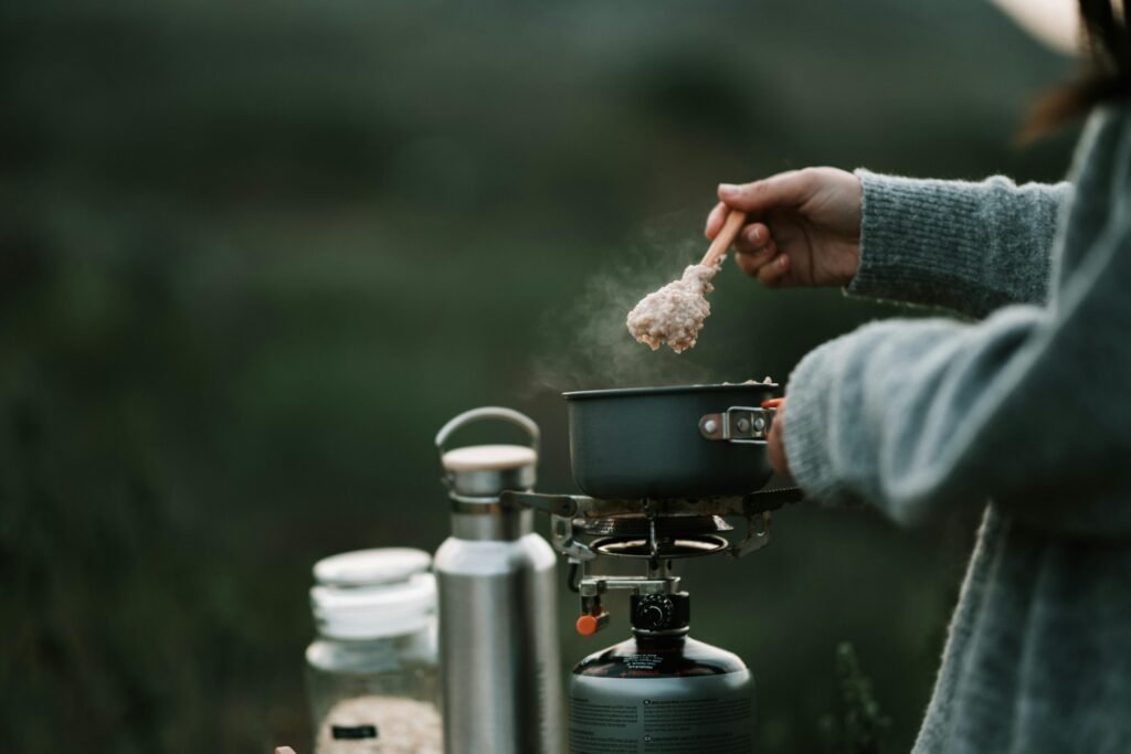 Camping food. A person is cooking steaming oatmeal on a portable stove during a camping trip.